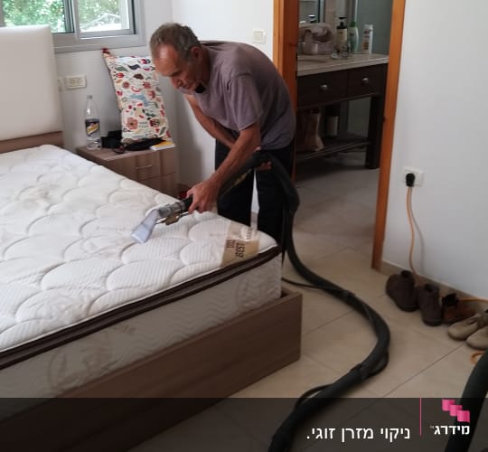 אדם מנקה מזרן עם מכונת ניקוי מיוחדת